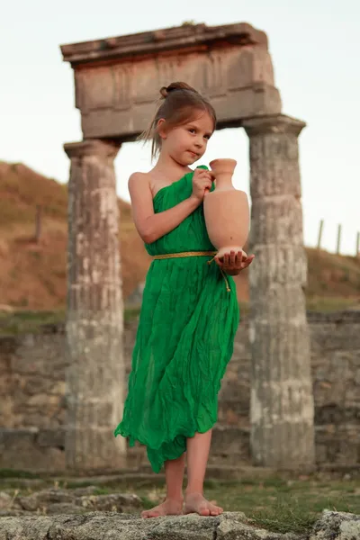 Красивая молодая греческая богиня в изумрудно-зеленом старинном платье, держащемся древней амфоры Стоковое Фото
