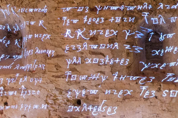 Светящийся античный руны символов и букв слов из огненного текста древние письмена на грубой каменной стены — стоковое фото