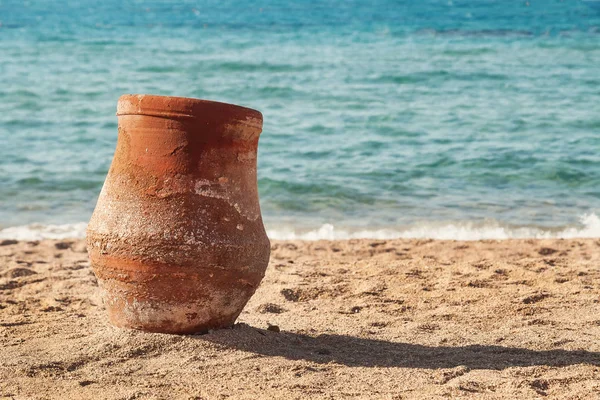 Старый земляной кувшин стоя на песке у моря Стоковое Фото